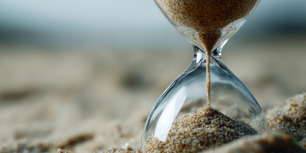 Close-up of sand running through an hourglass on a sandy surface, symbolising pause, reflection, and the timeless nature of quotes.