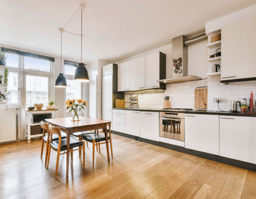 Bright modern kitchen with wooden dining table, pendant lights, white cabinets and warm natural light.