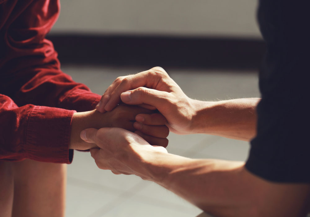 Close-up of one person holding another person’s hands in a supportive gesture.