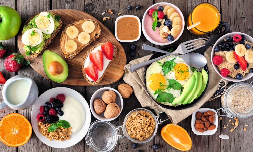 Healthy breakfast spread with eggs, avocado, fruit, yoghurt, oats, nuts and juice on a wooden table.