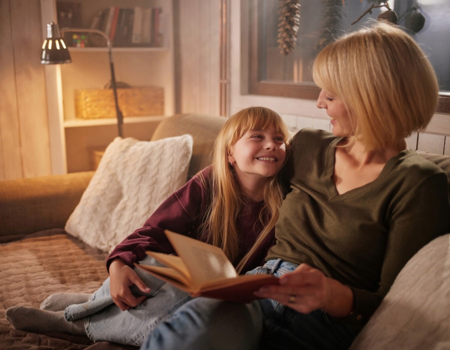 Woman and young girl sitting together on a sofa reading a book in a cosy room.