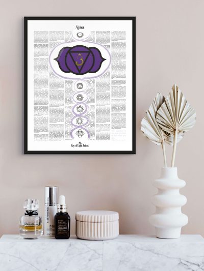 Ājñā third eye chakra print in a black frame above a marble cabinet, with skincare bottles, a lidded jar and a white vase of dried palm leaves.